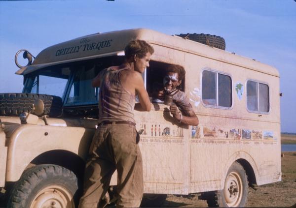 Two men chat next to a dusty old bus