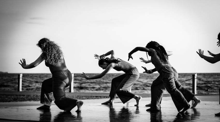 Dancers bend dramatically on a boardwalk overlooking open water