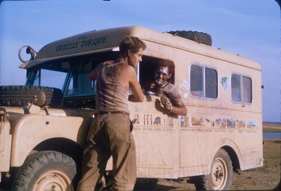 Two men chat next to a dusty old bus