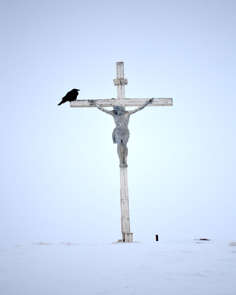 Statue of Jesus on a cross in the snow with a black crow perched 