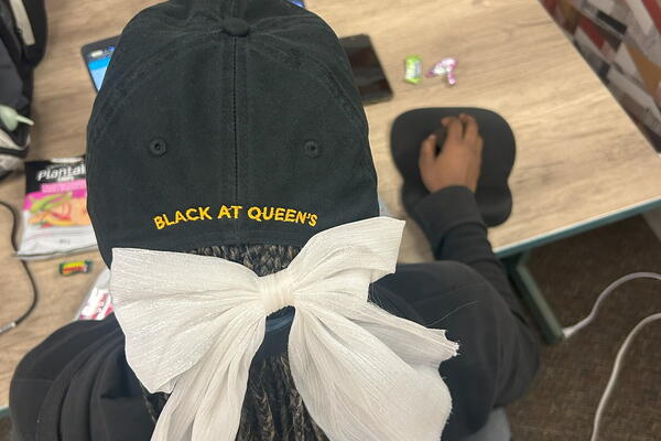 Overhead photo of a person wearing a baseball cap with "Black at Queen's" written on the back.