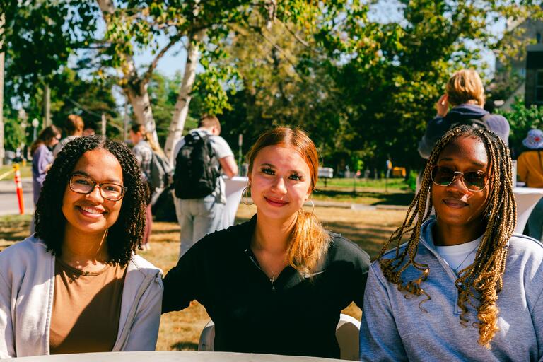 three people posing next to each other outdoors