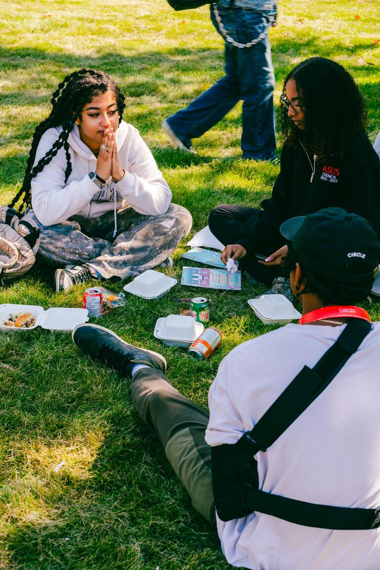 three people sitting in a circle on the ground with food and drinks near them
