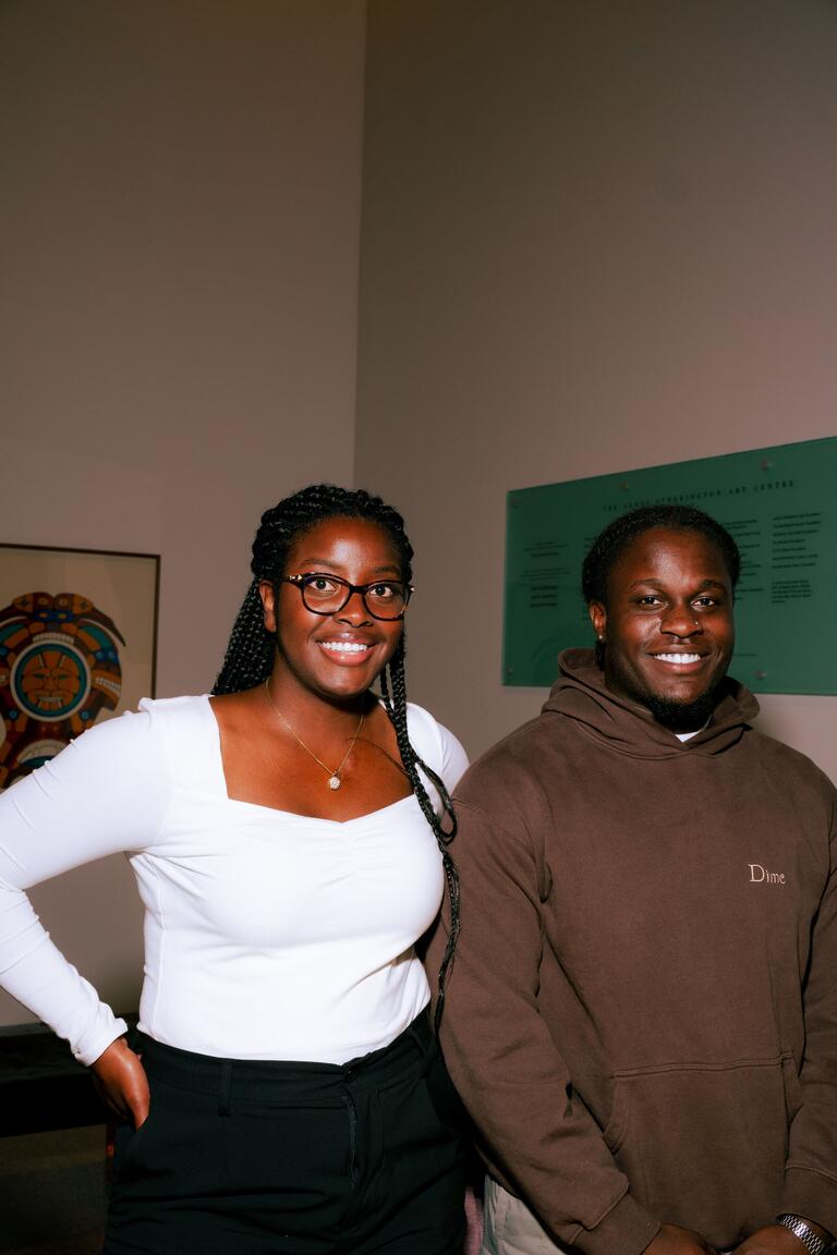 two people posing next to each other in front of a white wall
